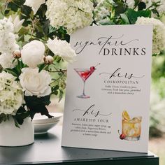 a table with a sign and flowers on it next to a glass filled with drinks