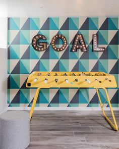 a yellow foosball table sitting in front of a wall with the word goal on it