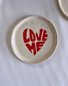 two plates with the words love me painted on them sitting on a white table cloth