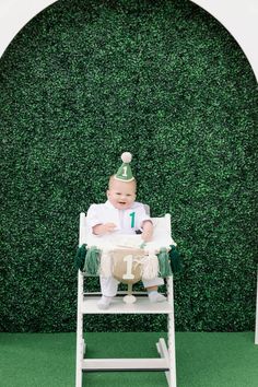 a baby sitting in a white chair with a green hat on it's head