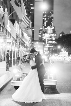 a bride and groom kissing in front of a car on a city street at night