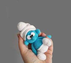 a hand holding a small crocheted blue and white stuffed animal in it's left hand