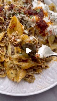 a white plate topped with pasta and meat covered in sauce, on top of a table