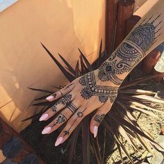 a woman's hand with henna tattoos on it and palm leaves in the foreground