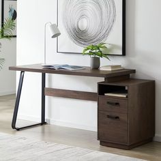 a wooden desk with two drawers and a plant on it in front of a white wall