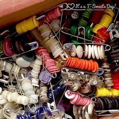 many different colored buttons and pins in a box with wooden frame on the bottom floor