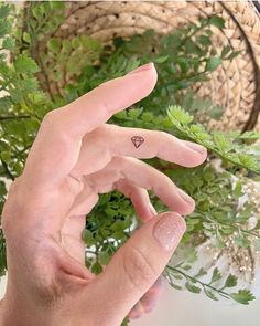 a person's hand with a tiny triangle tattoo on their left index finger next to a plant