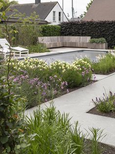 an outdoor garden with flowers and plants around the pool in front of a house on a cloudy day