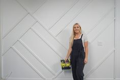 a woman standing in front of a white wall holding a tool box and smiling at the camera