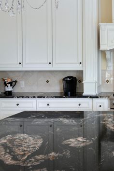 a kitchen with marble counter tops and white cabinets, chandelier hanging from the ceiling