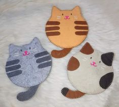 three felt cat coasters sitting on top of a white fur covered floor