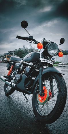 the motorcycle is parked on the pavement in front of some buildings and cloudy skys