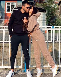 a man and woman standing next to each other in front of a fenced area