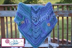 a blue crocheted blanket sitting on top of a wooden bench next to a fence