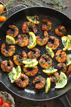 shrimp in a skillet with lemon wedges and herbs