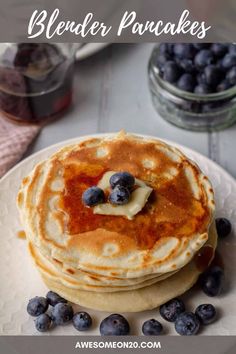 blueberry pancakes with butter and syrup on a white plate next to some blueberries