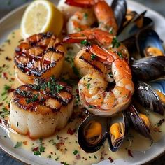 a white plate topped with shrimp, mussels and scallops next to a lemon wedge