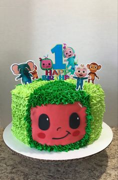 a birthday cake decorated with green grass and cartoon characters on the top is one year old