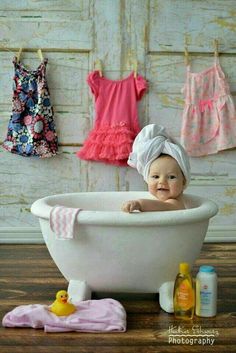 a baby sitting in a bathtub with clothes hanging on the wall