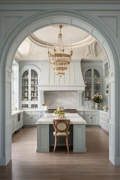 an archway leading into a kitchen with marble counter tops and white cabinets, along with a chandelier hanging from the ceiling