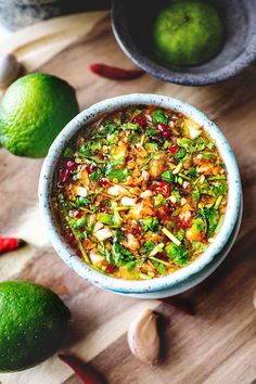 a bowl filled with food sitting on top of a wooden table next to limes