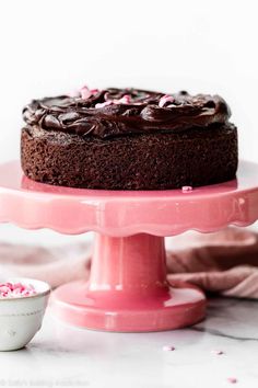 a chocolate cake with pink frosting and sprinkles on a pink cake stand