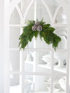 a christmas wreath is hanging on the window sill with pine cones and greenery