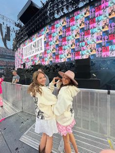 two girls standing in front of a giant screen at a music festival with their arms around each other