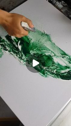 a person is using a brush to paint a green piece of art on a white surface