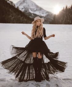 a woman standing in the snow wearing a black dress and hat