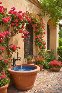 an outdoor fountain surrounded by potted plants and flowers on the side of a building