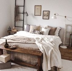 a bed with white sheets and pillows in a bedroom next to a ladder, lamp and pictures on the wall