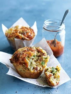 two muffins sitting on top of white paper next to a jar of sauce