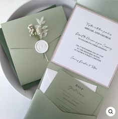 the wedding stationery is set on top of a white plate and green envelopes