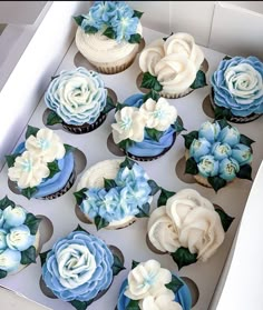 cupcakes decorated with blue and white frosting flowers in a box on a table