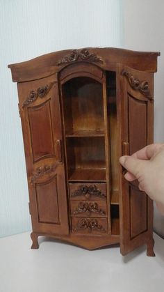 a hand is holding the door to a wooden cabinet that has drawers and doors on both sides