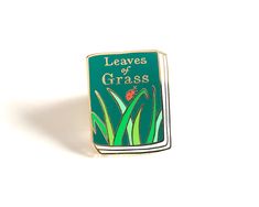 a green enamel pin with the words leaves of grass on it