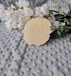 a white flower sitting on top of a bed next to a metal tag with the word reo inside