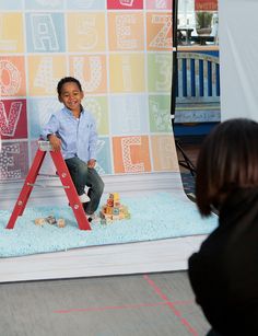 a little boy sitting on top of a red step ladder in front of a backdrop