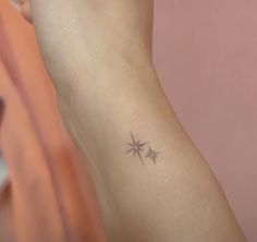 a small star tattoo on the left inner arm by someone's hand, in front of a pink wall