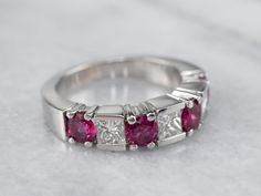 This ruby and diamond band has a sleek squared design that helps prevent it from spinning on your finger when worn. The classic combination of rubies and diamonds is elegant and feminine, and these sparkling gems are well protected in their prong and bezel settings. Perfect for an anniversary ring, this piece is also a great choice for someone who wants something a little more colorful than a traditional wedding band! Metal: 14K White Gold  Gem: 3 Diamonds totaling .86 Carats, I in Color, VS in Clarity, 4 Rubies totaling 1.19 Carats  Width of Band: 5.0 mm Height off Finger: 4.0 mm  Ring Size: 6 Marks: "GBG 14K" Stamped on the inside band Traditional Wedding Bands, Rubies And Diamonds, Diamond Half Eternity Band, Ruby Bands, Band Metal, Half Eternity Wedding Band, Half Eternity Band, Eternity Wedding Band, Ruby Diamond