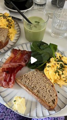 a plate with eggs, bacon and bread on it next to a glass of green juice