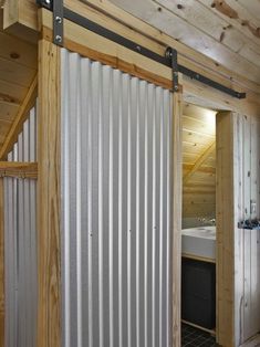 an open door leading to a bathroom with a bed in the corner and wooden walls