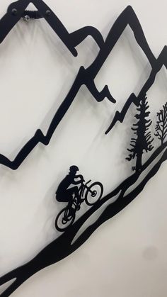 a metal mountain bike sculpture with trees and mountains in the background on a white wall