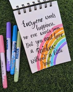 an open notebook with some writing on it next to three markers and a rainbow marker