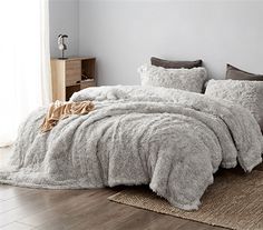 a bed covered in fluffy grey blankets and pillows