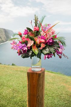 a vase filled with lots of flowers sitting on top of a wooden post next to the ocean