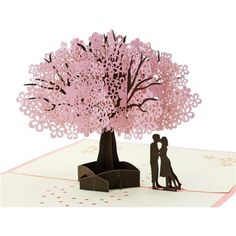 a couple kissing under a pink tree on top of a card