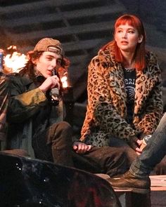 two people sitting next to each other in front of a fire pit with flames coming out of them