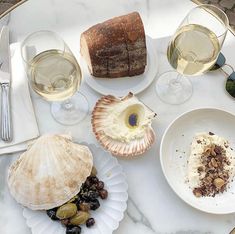 an assortment of food and wine on a marble table top with glasses of white wine